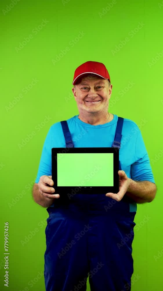 Repairman in overalls showing tablet with horizontal green screen and smiling. Repairman in overalls showing tablet with horizontal green screen and smiling.