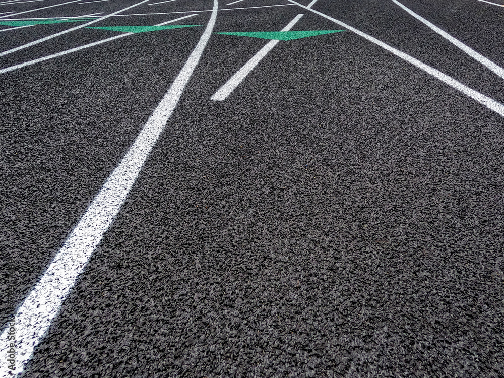 Track and Field Running Lanes. Overhead view of a rubber black running surface with white lane lines. There is a slight curve of the white lane lines. Colored lane markers can be seen in the distance.