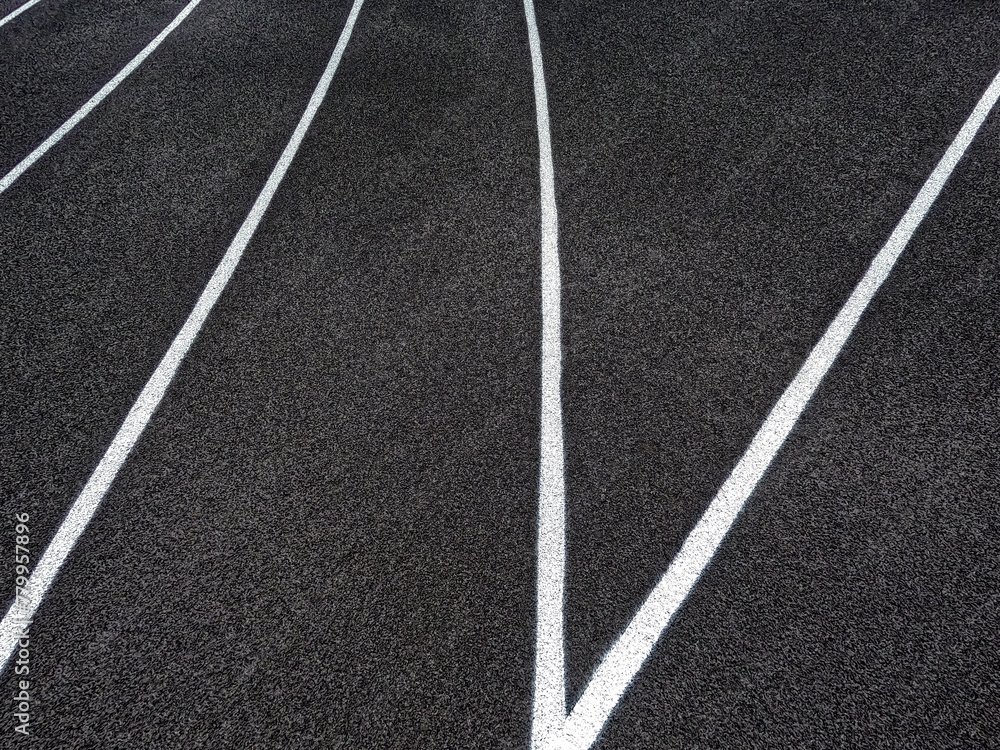 Track and Field Running Lanes. Overhead view of a rubber black running track surface with white lane lines. The lane lines create beautiful geometric shape patterns.