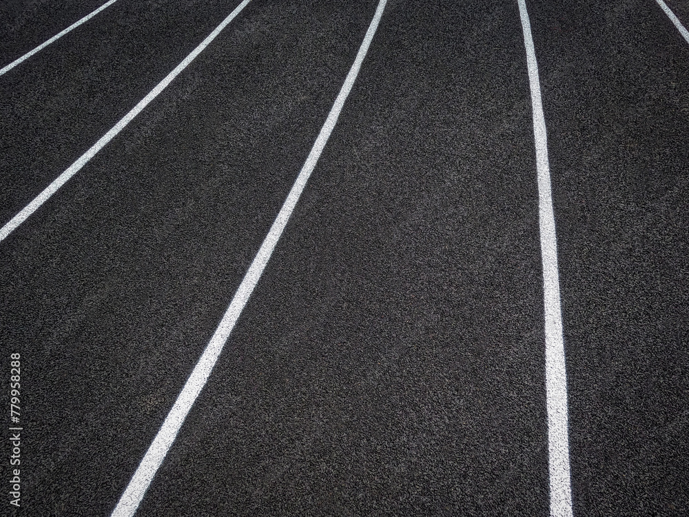 Fototapeta premium Track and Field Running Lanes. Overhead view of a rubber black running surface with white lane lines. There is a slight curve of the white lane lines. 