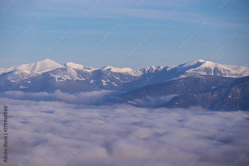 Obraz premium Scenic view on snow capped mountain peaks of Nocky Mountains and High Tauern. Hiking trail in Karawanks, Carinthia, Austria, Europe. Winter wonderland in Austrian Alps. Valley covered by thick fog
