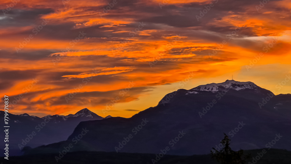 Fototapeta premium Scenic view of snow capped mountain peak Dobratsch at sunset seen from Taborhoehe in Carinthia, Austria, Europe. Sky has vibrant orange and pink colors with clouds swirling around summit. Serenity
