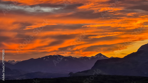 Scenic view of snow capped mountain peak Dobratsch at sunset seen from Taborhoehe in Carinthia  Austria  Europe. Sky has vibrant orange and pink colors with clouds swirling around summit. Serenity