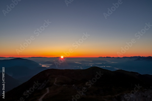Panoramic sunrise view from Dobratsch on the Julian Alps and Karawanks in Austria, Europe. Silhouette of endless mountain ranges with orange and pink colors of sky. Jagged sharp peaks and valleys