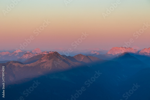 Panoramic sunrise view from summit Dobratsch on Julian Alps and Karawanks in Austria, Europe. Silhouette of endless mountain ranges with orange and pink colors of sky. Jagged sharp peaks and valleys