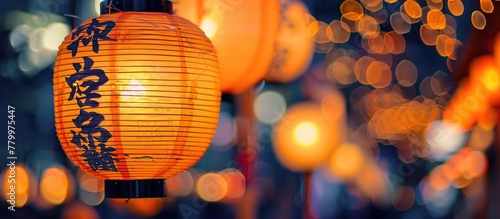 A Japanese-style close-up shot of orange-yellow glowing lanterns at night hanging by the roadside with a blurred bokeh background. Space to add text. © Mas