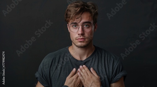 A man with glasses and a beard is standing in front of a black background. He is wearing a black shirt and has his hands clasped together