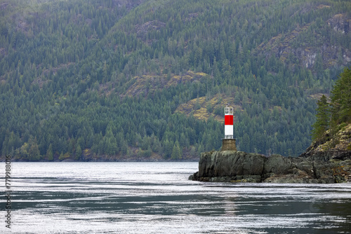 Red and white lighthouse stands in the water, guiding ships with its beacon
