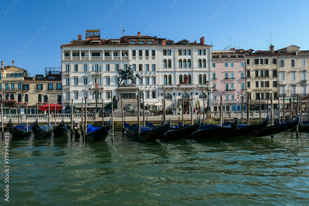 Gondolas parked in front of Londra Palace Venezia near San Marco square, Venice, Veneto, Northern Italy, Europe. Massive statue landmark in front of the building. Discover the Venetian Lagoon