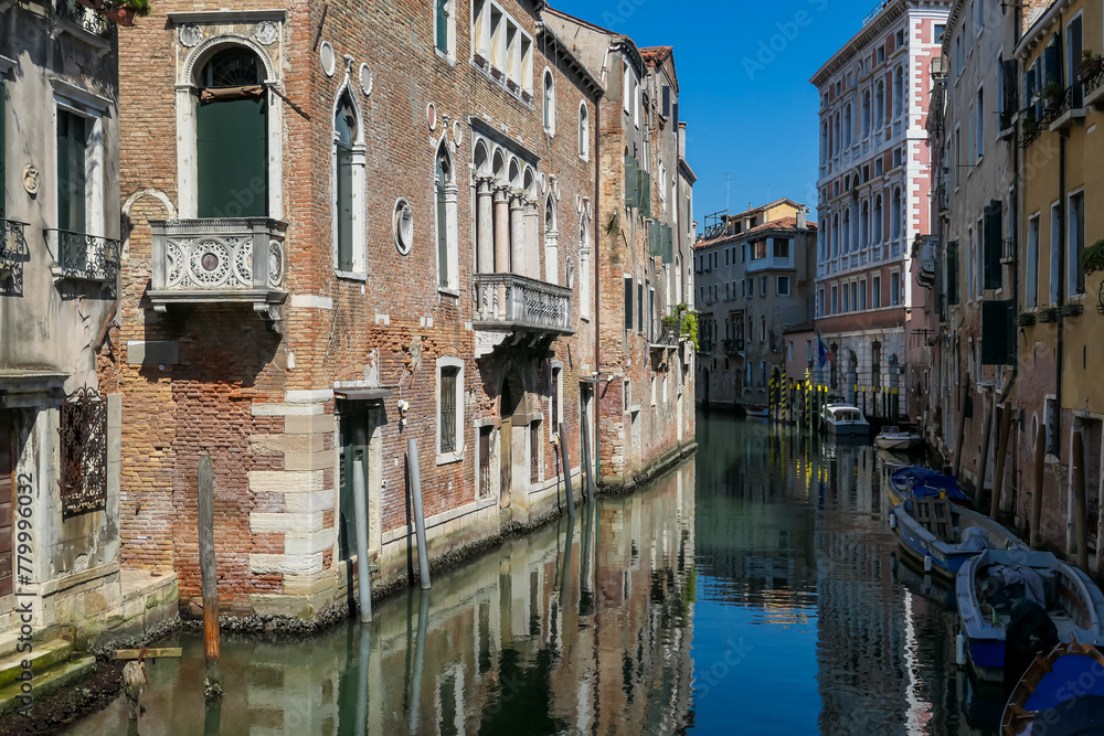 Floating boats with panoramic view of a water channel in city of Venice, Veneto, Italy, Europe. Venetian architectural landmarks and old houses facades along water canal. Urban tourism in summer