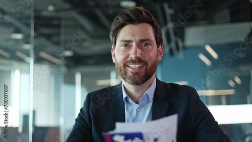 Portrait of caucasian man checking brochures in hands and looking at camera with satisfied facial expression. Pleased male getting interested in advertisement received by mail in working space. photo