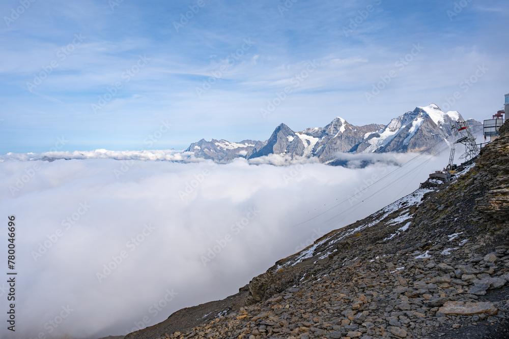 View of Swiss Alps over clouds on a bright sunny day from Schilthorn summit in Switzerland. Cable car pylon