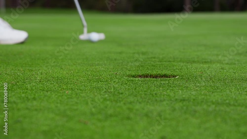 Close shot at ground level of a golfer on a carefully maintained putting green, the golfer putts the golf ball but misses the hole.