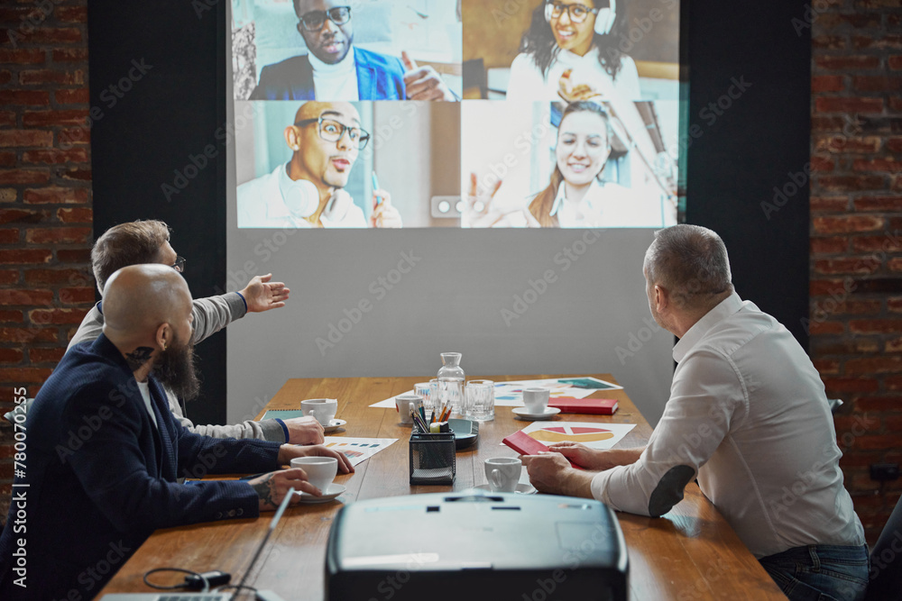 Group of employees, projects managers having online video call on tv screen monitor in conference room. Project discussion with team. Concept of business, teamwork, cooperation with colleagues