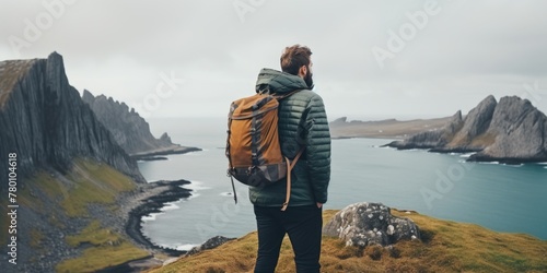 A man wearing a green jacket stands on a rocky hill overlooking a body of water