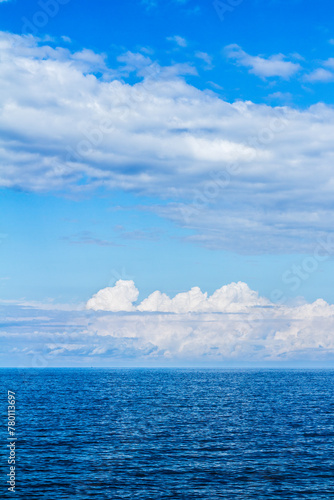 Bodies of cumulus thunderstorm clouds over ocean waters horizon line in blue sky background.