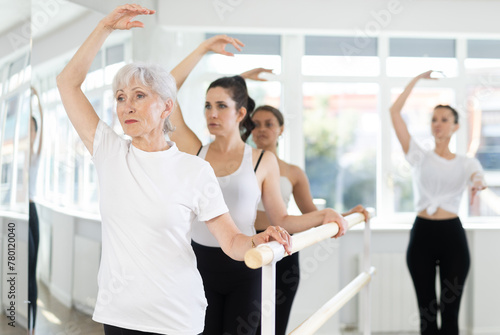 Experienced choreographer teaches ballet dancers movements at ballet barre in a choreographic studio