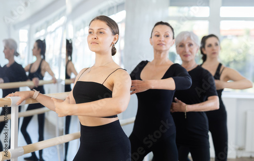 Group of women rehearsing plie ballet movement at barre in dance studio