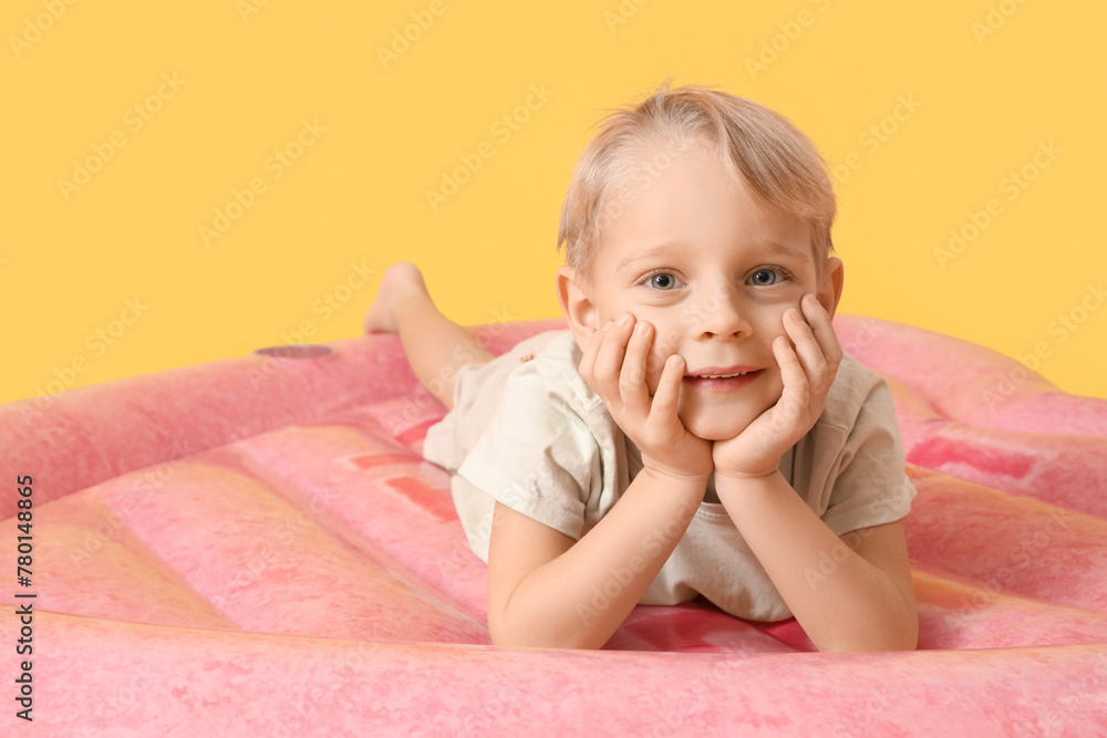 Cute little boy lying on swim mattress against yellow background Cute little boy lying on swim mattress against yellow background