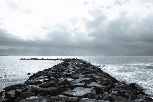 Tranquil monochrome image showcasing a majestic stone pier gracefully stretching into the tumultuous ocean as powerful waves crash against it, evoking a sense of serenity and awe.