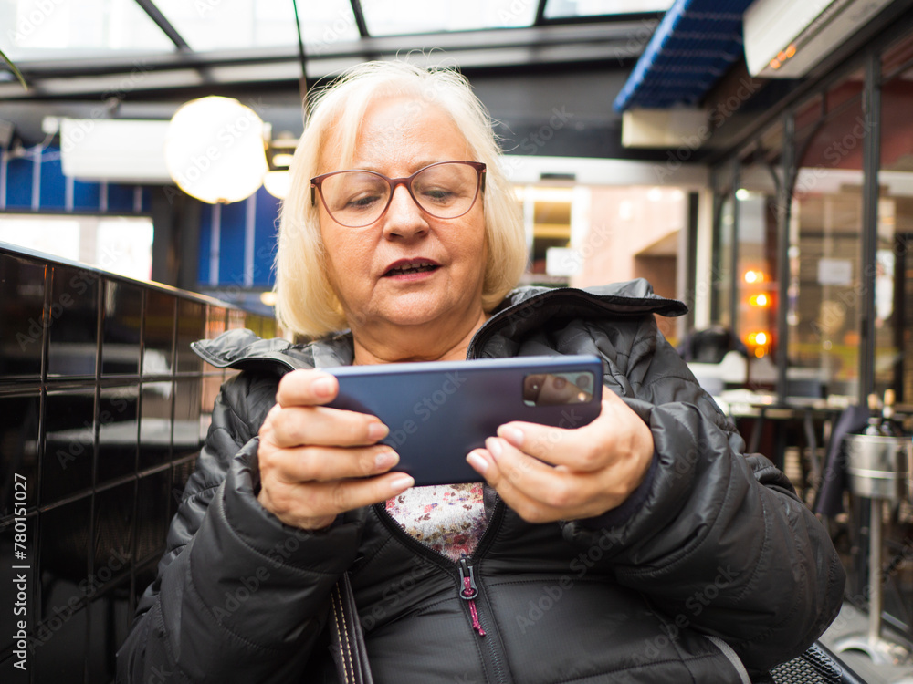 gamer grandmother playing on the mobile phone on a restaurant terrace gamer grandmother playing on the mobile phone on a restaurant terrace
