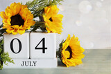 United States Independence Day. White wood calendar blocks with the date July 4th and beautiful sunflower bouquet with bokeh. Selective focus with blurred background. 