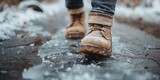 A close-up of brown winter boots stepping into a puddle of water, creating ripples