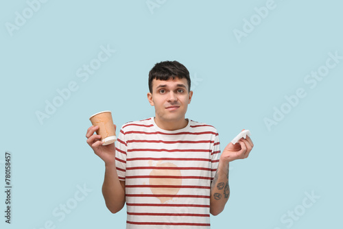 Confused young man with coffee stains on his t-shirt on blue background