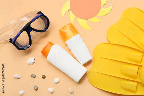 Bottles of sunscreen, diving mask and flippers on orange background