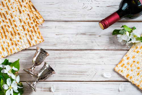 Jewish religious holiday of Passover. Bottle of wine, matzo and flowers on white wooden background.