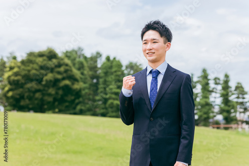 公園でガッツポーズする若いビジネスマン（やる気・応援・意欲・フレッシャーズ・新社会人） 