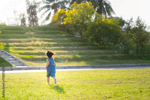 Portrait of Asian Child girl enjoy outdoor playtime amidst nature, running on green grass in the park, rear back view, in summer or spring time, run in the green fields, close to nature. © Kanthita