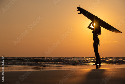 Silhouette sexy beautiful Asian model wearing bikini swimming suite posing happy on beach with surfboard is water sport game and hobby leisure in summer holiday lifestyle with sunset sky background.