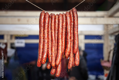Selective blur on cajna kobasica sausages spiked for sale hanging on a stand of a serbian market. Cajna kobasica, or tea sausage, is a traditional serbian sausage made of smoked cured pork. photo