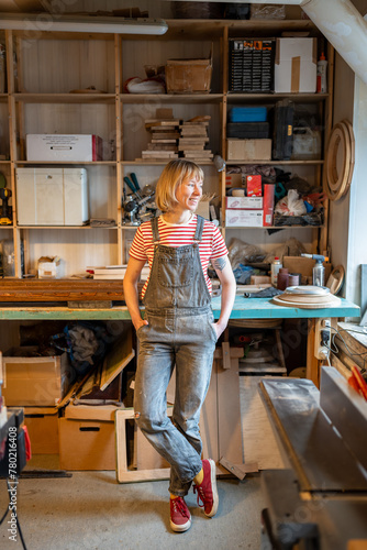 Pleased thoughtful woodworker woman take break in carpentry workshop smiling looking to window pondering creative project. Pleased joiner female relaxed standing in artisan room daydreaming. photo