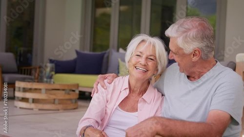 Loving senior couple sitting outdoors relaxing on deck at home laughing together - shot in slow motion