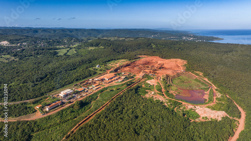 aerial landscape view around a Bauxite mining plant located within a green forest with ocean in the background and orange surface around the mine