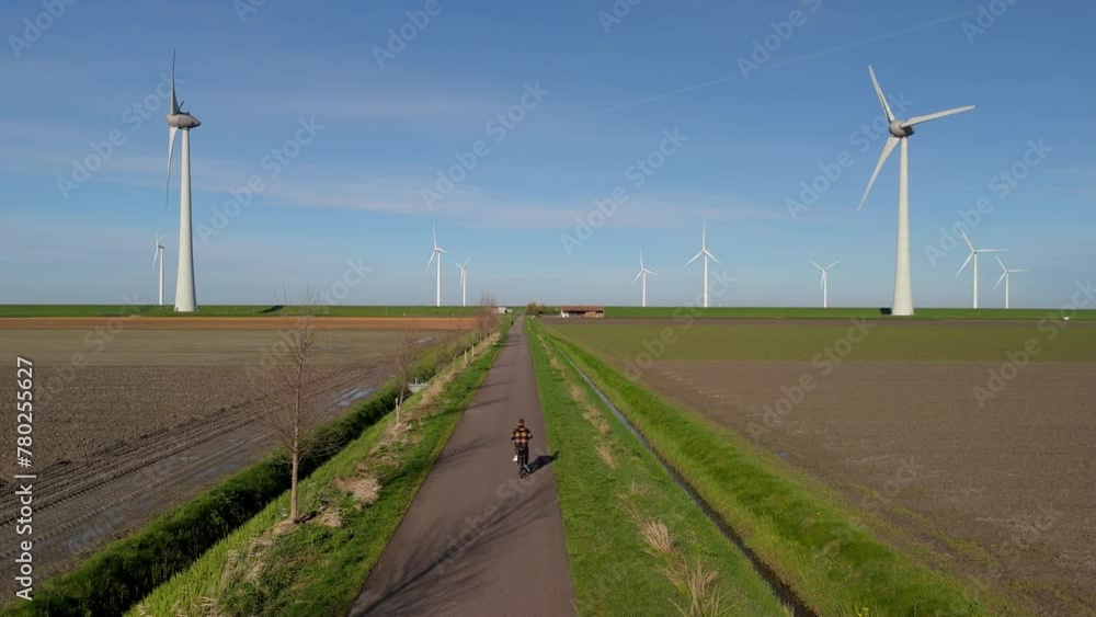 a young man on an electric green bike bicycle by a windmill farm windmills isolated on a beautiful bright day in Netherlands Flevoland Noordoostpolder, men bicycle countryside on a green electric bike a young man on an electric green bike bicycle by a windmill farm windmills isolated on a beautiful bright day in Netherlands Flevoland Noordoostpolder, men bicycle countryside on a green electric bike