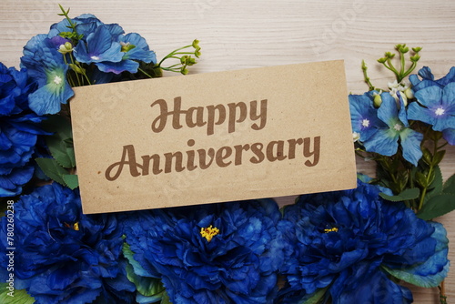 Happy Anniversary text message on paper card with flowers border frame on wooden background