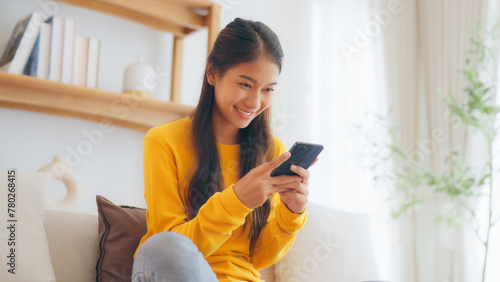 Happy young asian woman relax on comfortable couch at home, typing chat message on smartphone, smiling girl use cell phone chatting, searching information on browser wireless internet, online shopping © Monster Ztudio