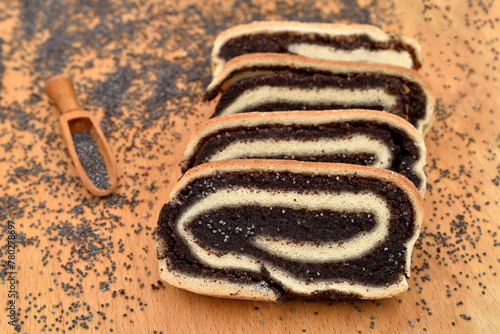 Slices of homemade poppy seed roll with wooden scoop and poppy seeds on the wooden board. Selective focus. 