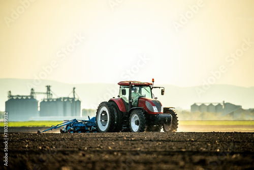 Farmer operates a red tractor, seeding the field against the backdrop of a setting sun