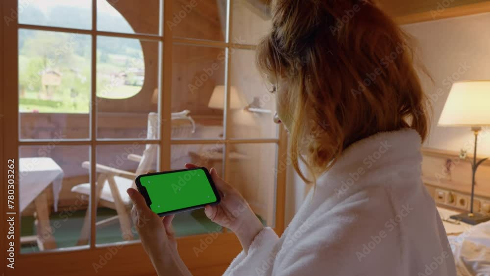 Green screen chroma key phone held by woman while wearing bathrobe in the morning. Female watching something on smartphone sitting in bed. Green screen chroma key phone held by woman while wearing bathrobe in the morning. Female watching something on smartphone sitting in bed.