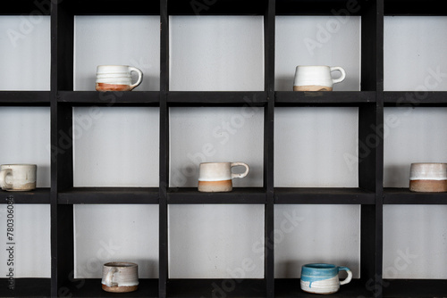 Assorted artisanal mugs display on a black shelf unit against a neutral wall showcasing minimalist design and pottery craft from handmade