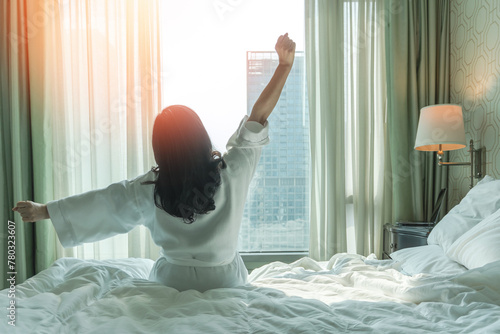 Hotel relaxation on lazy day with Asian woman waking up from good sleep on bed in weekend morning resting in comfort bedroom looking toward city view, having happy, work-life quality balance lifestyle © Chinnapong