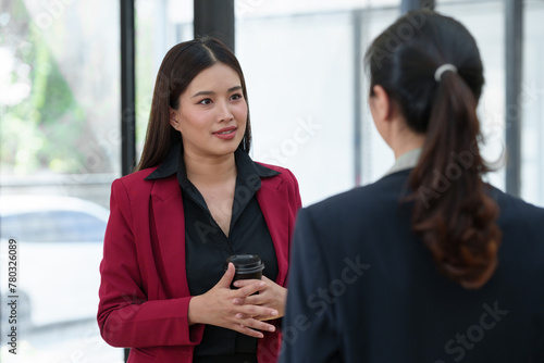 Two Asian businesswomen are discussing a new business project in the office. holding a drink Relaxing conversation, online business concept Starting a new business.