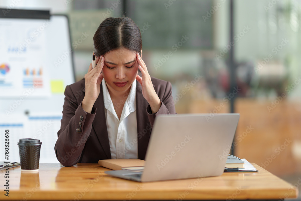 Asian businesswoman who is tired has a headache, is stressed, sleepy, angry, and bored from sitting at a desk for a long time doing contact work. online business on laptop Office syndrome concept. Asian businesswoman who is tired has a headache, is stressed, sleepy, angry, and bored from sitting at a desk for a long time doing contact work. online business on laptop Office syndrome concept.