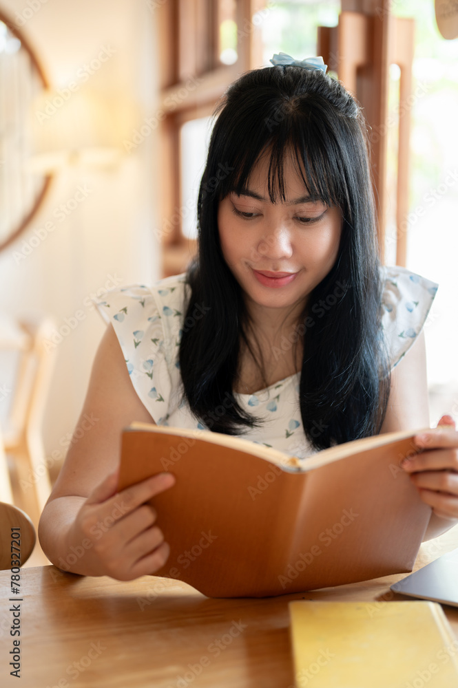 A relaxed and positive young Asian woman reading a book in a beautiful coffee shop on a bright day. A relaxed and positive young Asian woman reading a book in a beautiful coffee shop on a bright day.