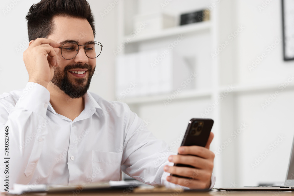 Handsome young man using smartphone at table in office Handsome young man using smartphone at table in office