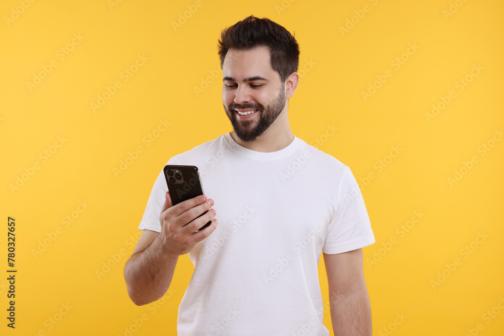 Happy young man using smartphone on yellow background Happy young man using smartphone on yellow background